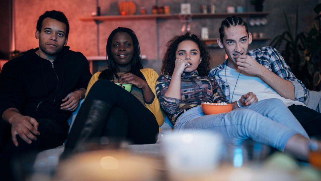 Group of people sitting together on a sofa watching TV.