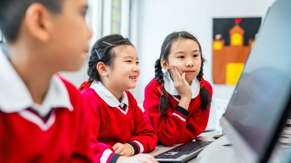 A group of young school children looking at a computer.