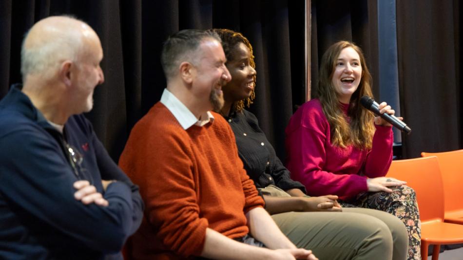 Four people speaking on a panel at a conference, the person at the end is holding a microphone.