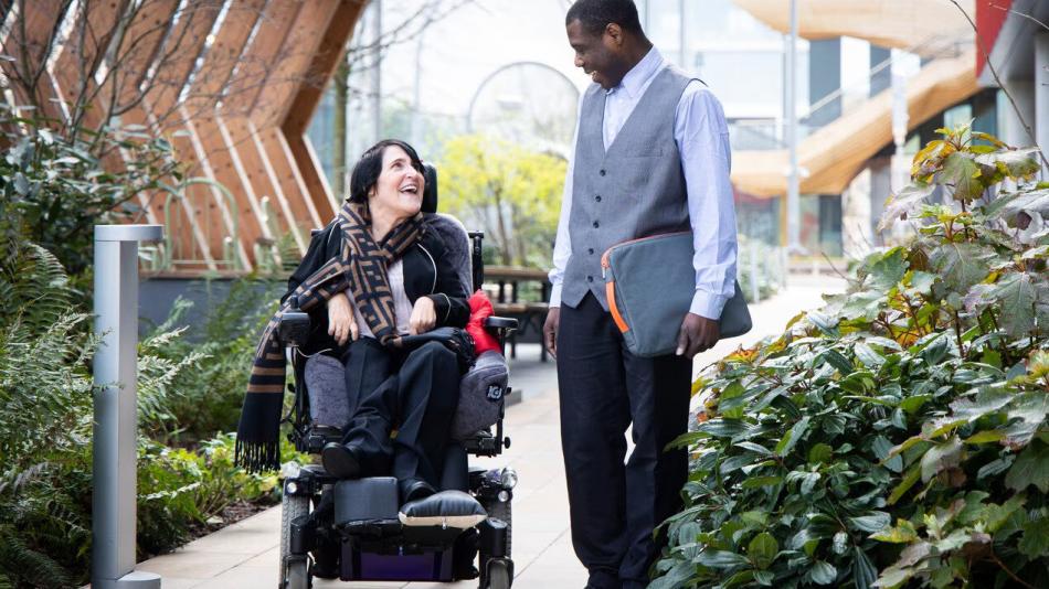 An employee in a wheelchair chatting to a colleague walking towards the office