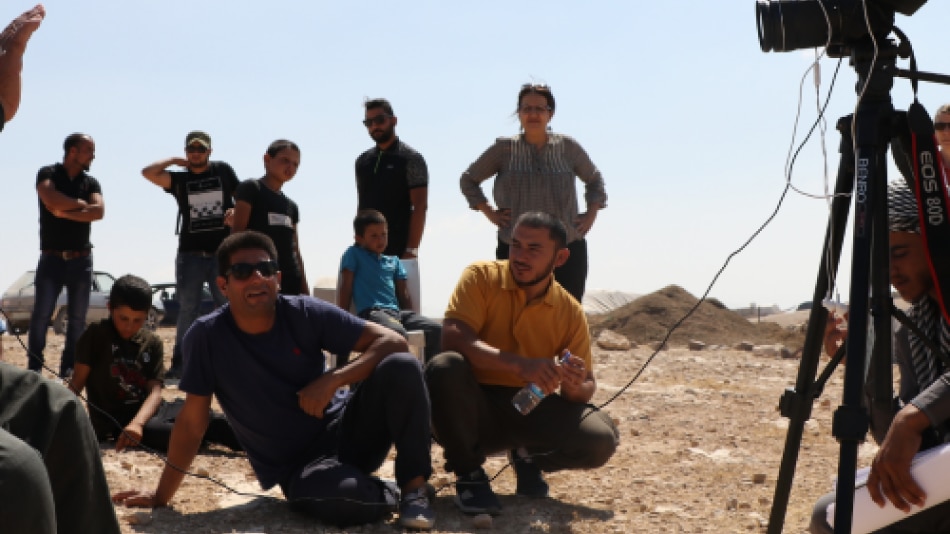 A group of people sitting in front of a camera in a desert landscape.