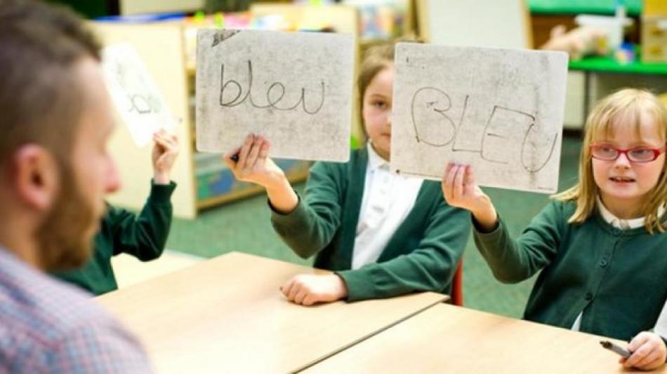 Young female pupils holding up French signs in front of male teacher