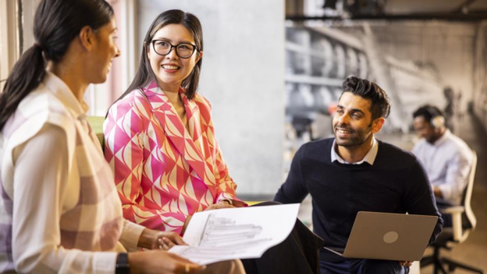 A group of young people - two women and a man - talking to each other inside an office