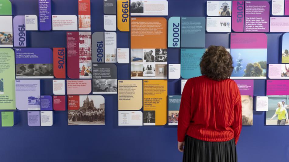 A woman looking at a wall displaying a large number of colourful posters