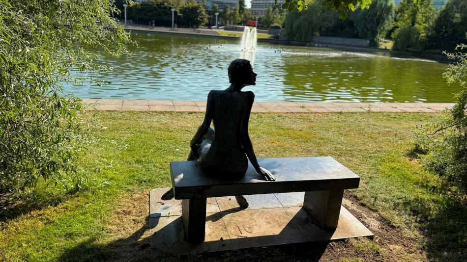 A metal sculpture sat on a bench at University College Dublin overlooking a lake