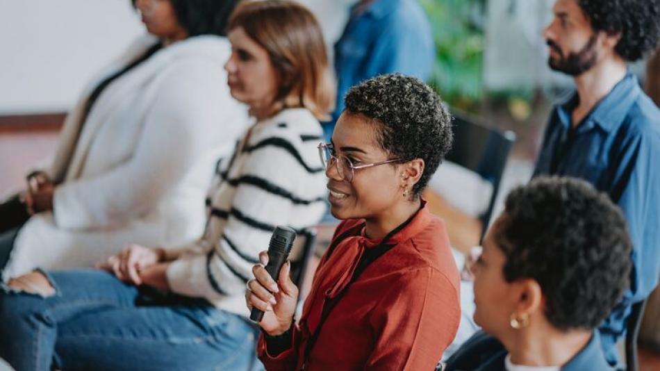 An individual is speaking in a mic while others listen