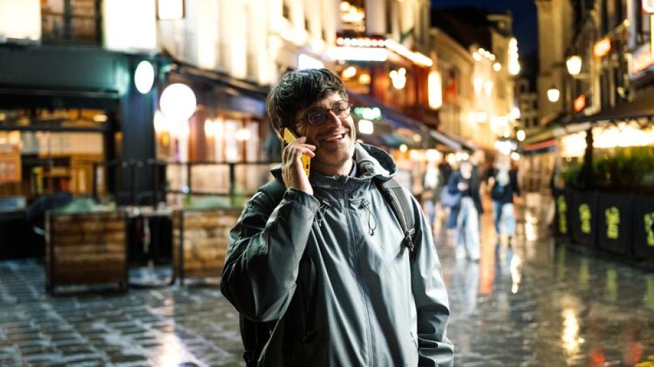 Man using smart phone in the old city street at night, talking on the phone and smiling
