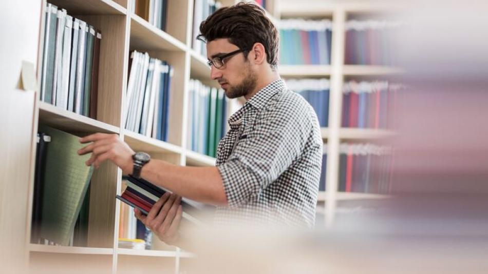 Man in a library taking a book from a shelf