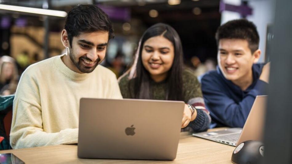 Three students sitting next to each other looking at a laptop.