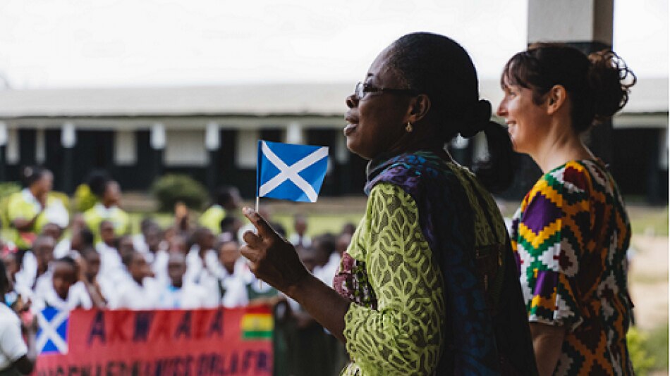 Two ladies, on Ghanaian and one Scottish address students at an outdoor assembly in Ghana